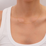 Gold necklace with a small pavé diamond horseshoe charm  on a person wearing a white top against a neutral background