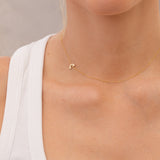 Gold necklace with a small rainbow charm  worn by a person against a neutral background