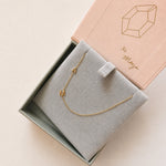 Gold necklace with 'A' and M' pendant in a jewelry box with 'xo Maya' branding.