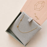Gold necklace with 'A' and M' pendant in a jewelry box with 'xo Maya' branding.