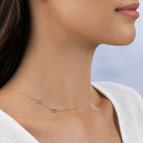 Gold necklace with small letter pendants on a person wearing a white top against a light blue background