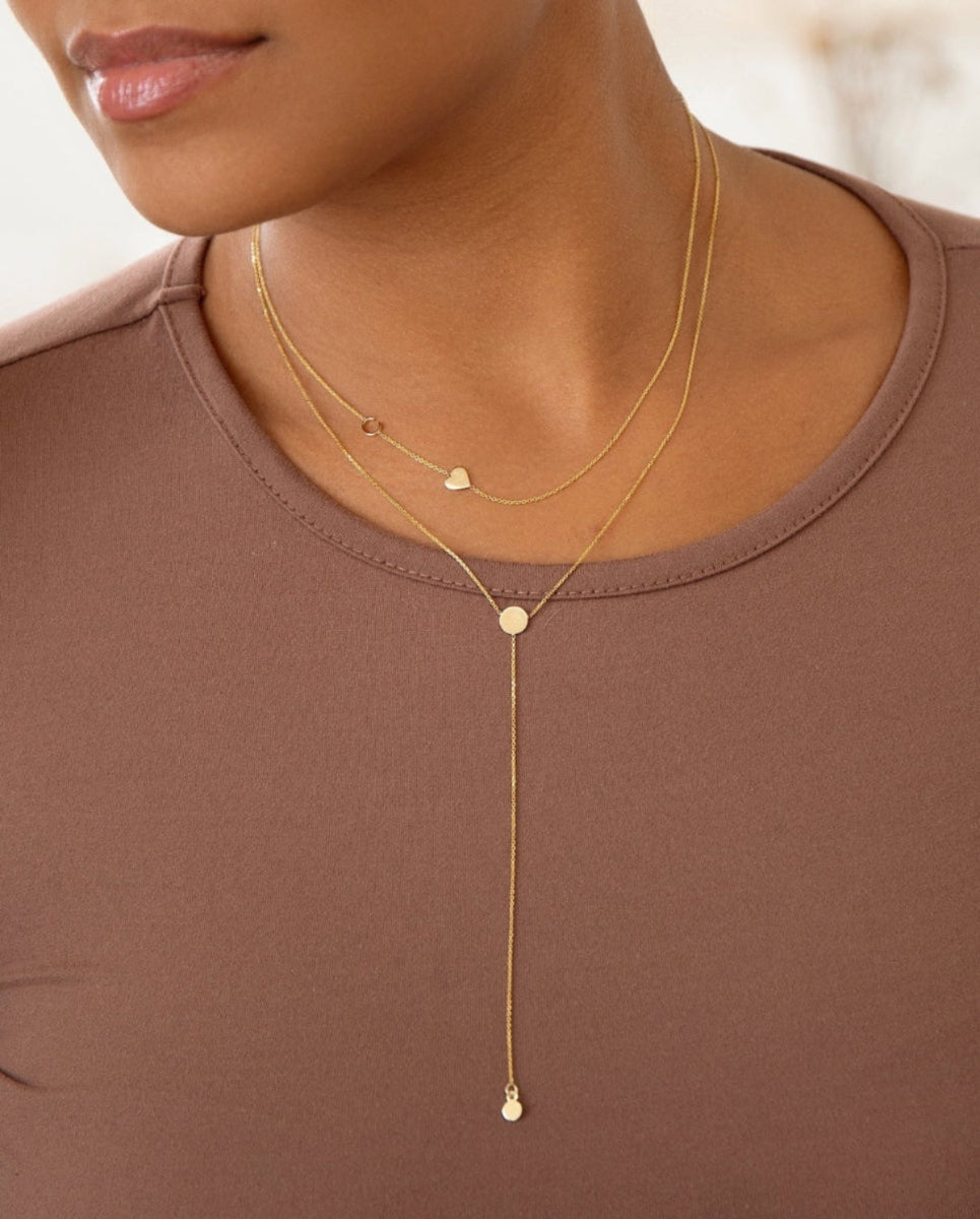 Gold necklace with heart pendant on a person wearing a brown top