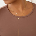 Gold necklace with heart pendant on a person wearing a brown top