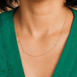Gold necklace with letter 'M' pendants on a person wearing a green top.