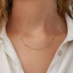 Gold necklace with small charms on a person wearing a white shirt.