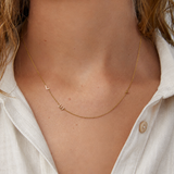 Gold necklace with small charms on a person wearing a white shirt.