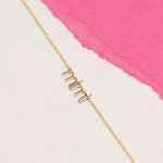 Gold 'mimi' necklace on a white and pink background