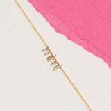 Gold 'mimi' necklace on a white and pink background