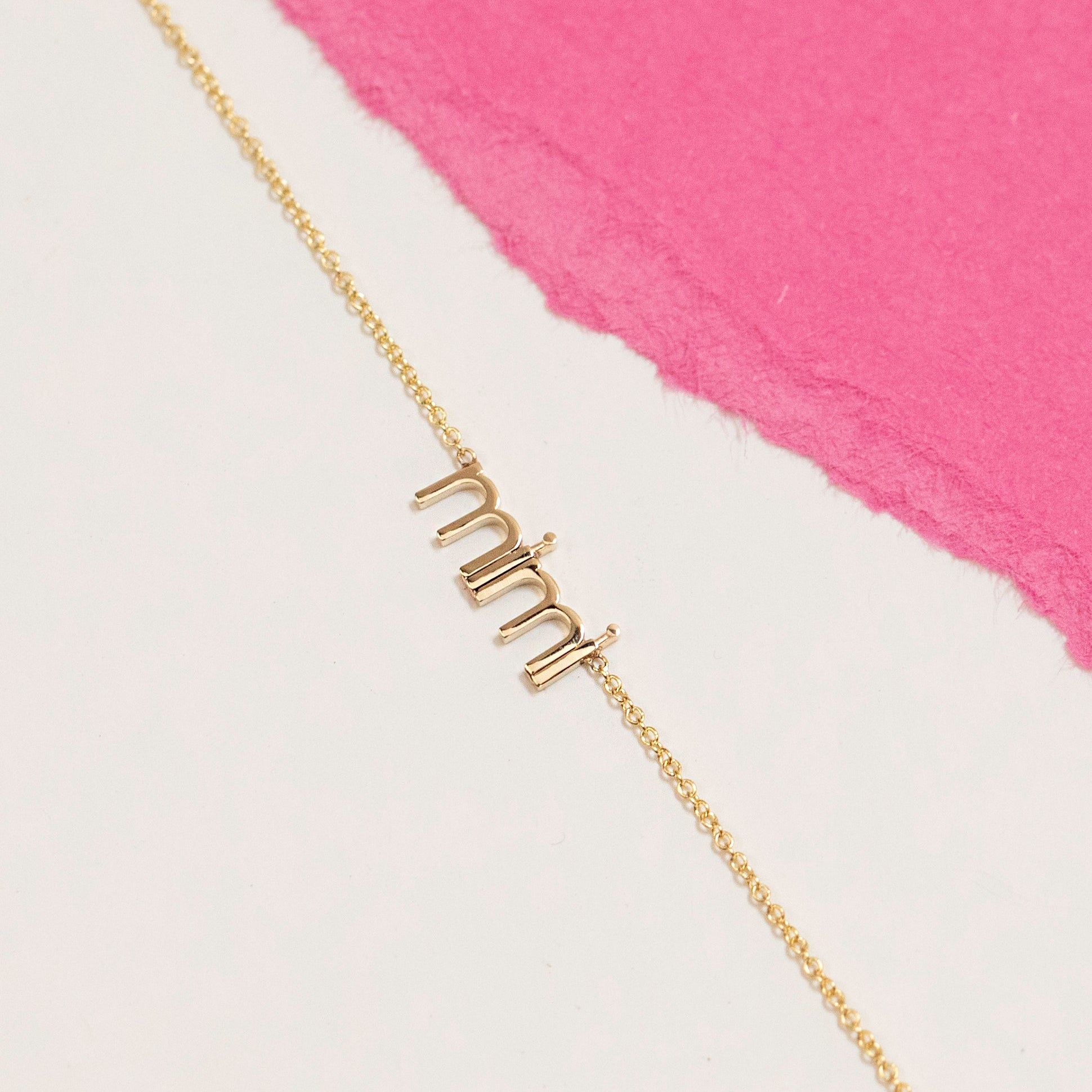 Gold 'mimi' necklace on a white and pink background