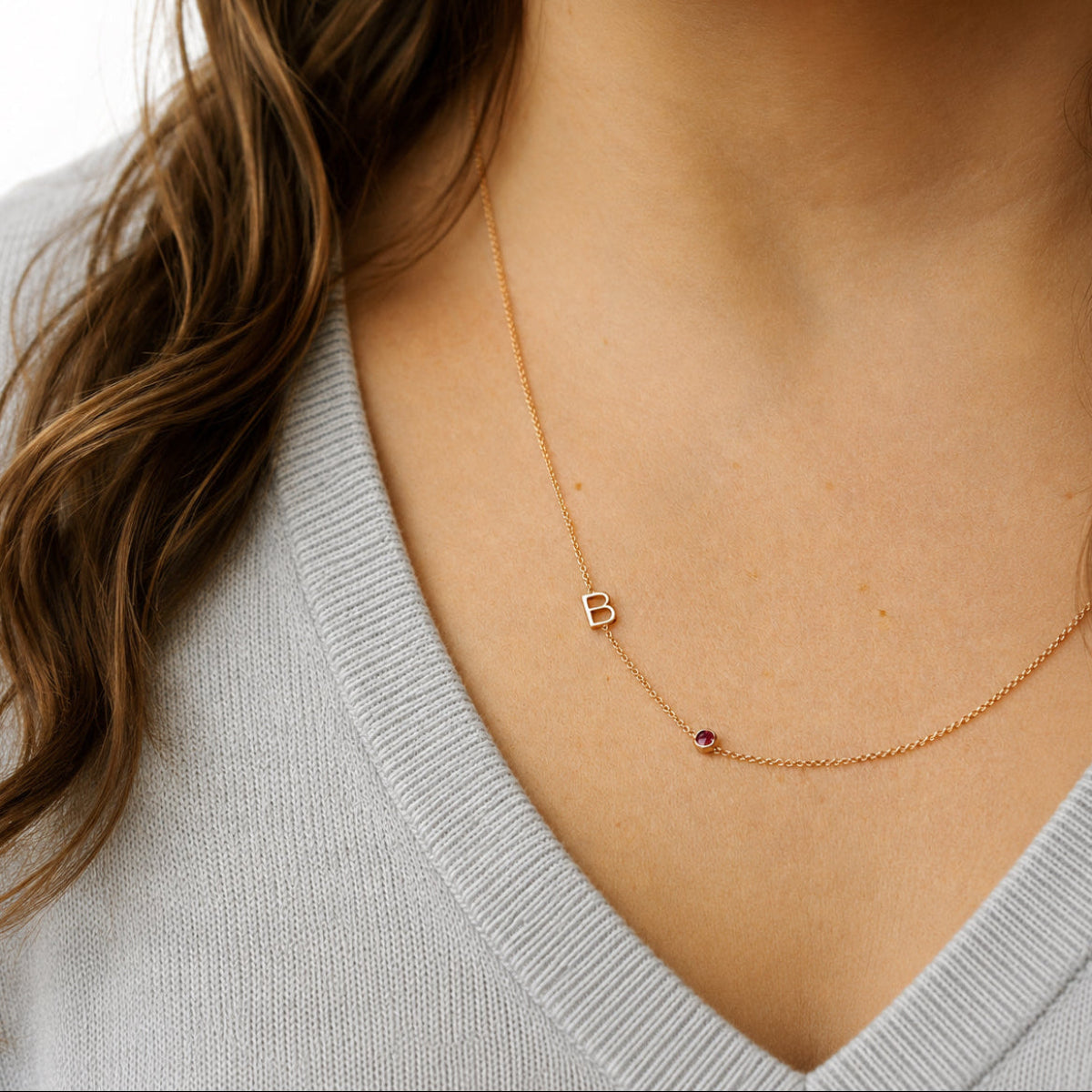 Gold necklace with a letter 'B' pendant on a person wearing a light gray sweater.