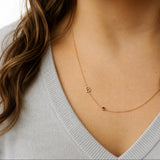 Gold necklace with a letter 'B' pendant on a person wearing a light gray sweater.