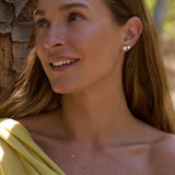 Woman wearing diamond stud earrings and a necklace, with a blurred natural background