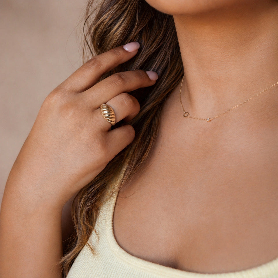 Close-up of a person wearing a gold ring and necklace against a neutral background