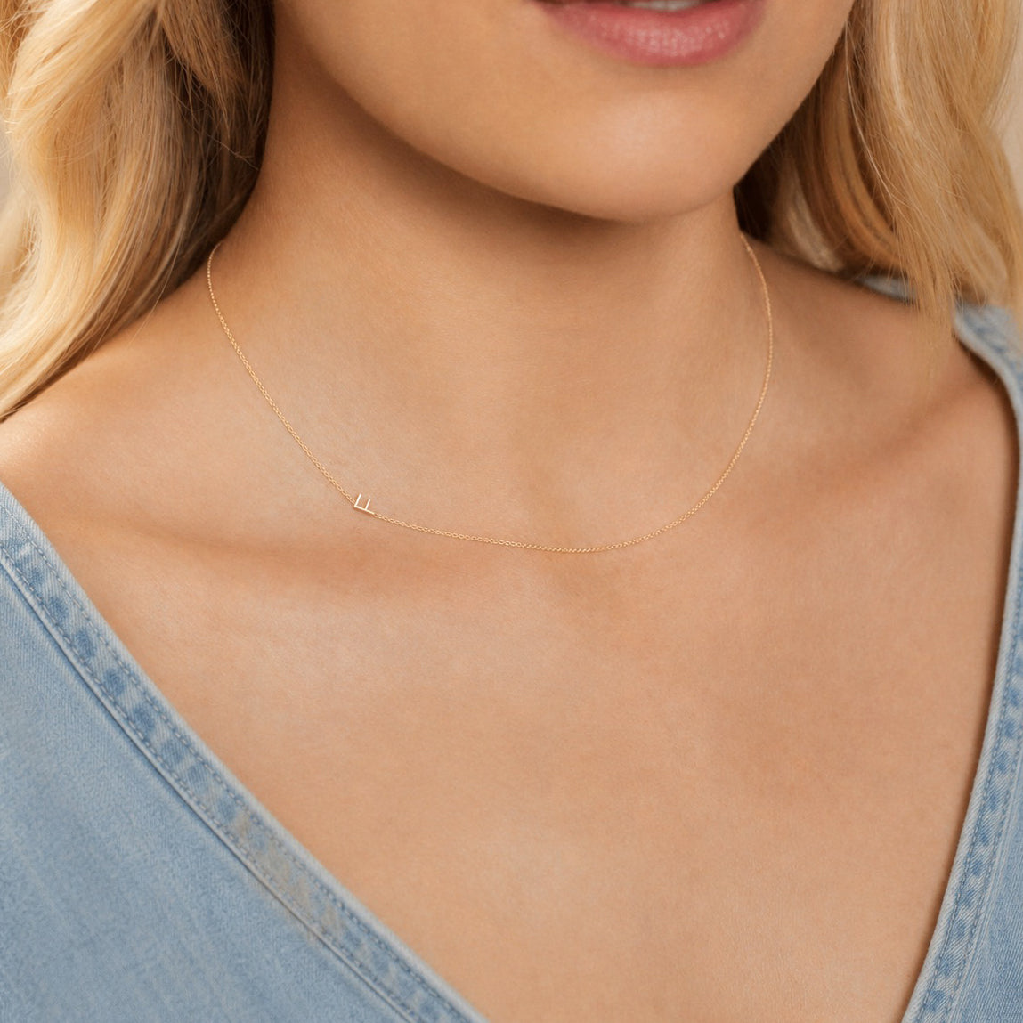 Close-up of a woman's neck wearing a gold necklace with a letter F charm. 