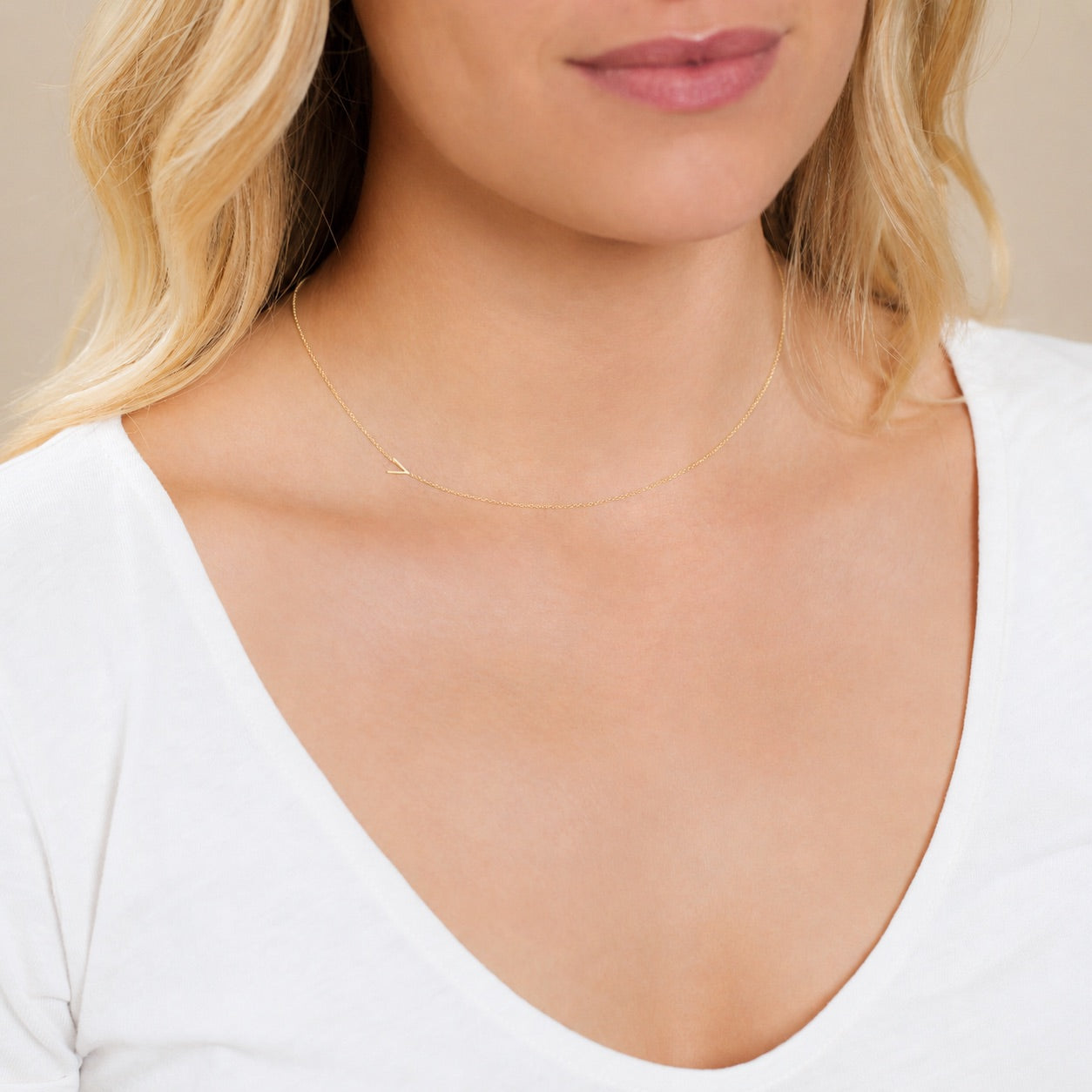A close-up of a woman's neck wearing a yellow gold necklace with a letter V charm.