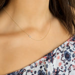 A close-up of a woman’s neck area wearing a yellow gold necklace with a letter S charm and a patterned off-shoulder top.