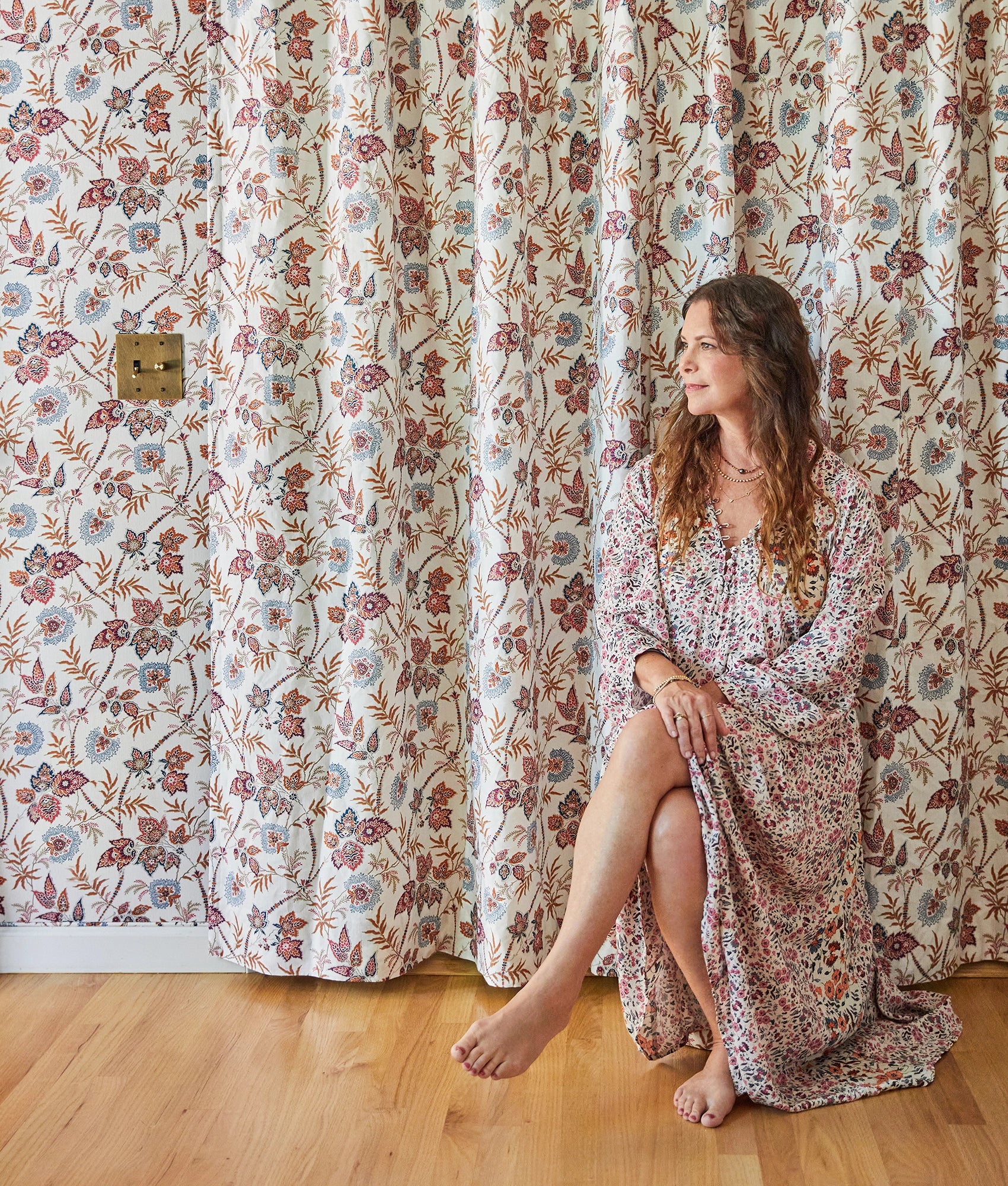 Woman in a floral dress sitting in front of a floral curtain