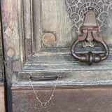 Necklace draped over an ornate metal door knocker on a wooden door.