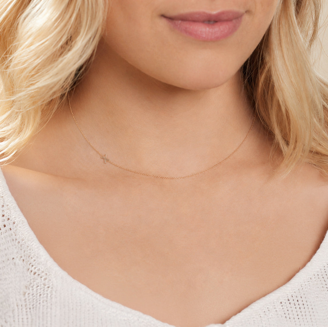 A close-up of a woman's neck wearing a white gold necklace with a letter X charm.