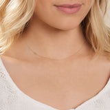A close-up of a woman's neck wearing a white gold necklace with a letter X charm.