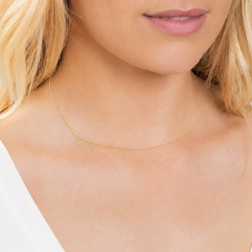 Close-up of a person wearing a delicate gold necklace with a letter Y charm.