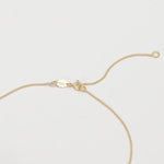 The back of a necklace in yellow gold on an off-white background. 