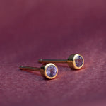 Gold earrings with purple gemstones on a maroon background