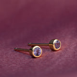 Gold earrings with purple gemstones on a maroon background