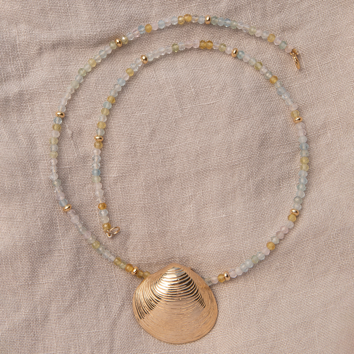 An Endless Summer Necklace - Saint-Tropez with The Golden Venus Shell on a beige fabric background. 