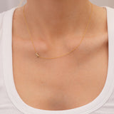 Gold necklace with a small pavé diamond ribbon charm on a person wearing a white top.