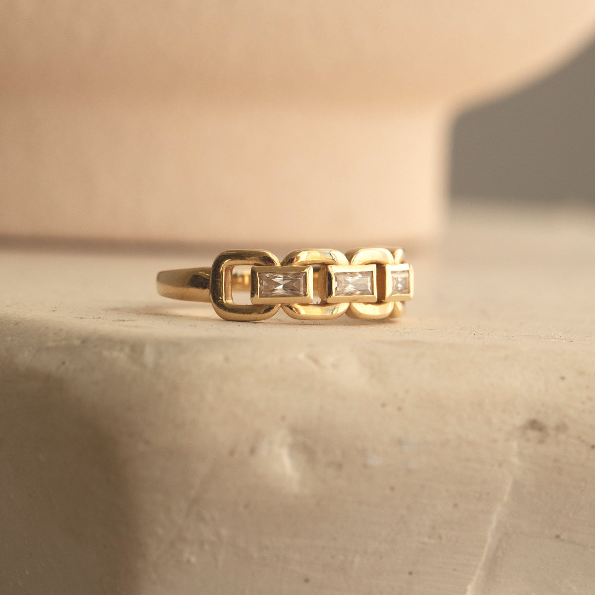 A yellow gold  C'est Moi Link Ring on a cream textured surface. 