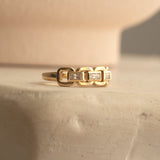 A yellow gold  C'est Moi Link Ring on a cream textured surface. 