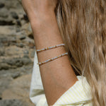 Close-up of a woman’s arm wearing two Endless Summer Bracelets – Saint-Tropez, shown next to blonde hair with a stone blurred background.