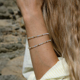 Close-up of a woman’s arm wearing two Endless Summer Bracelets – Saint-Tropez, shown next to blonde hair with a stone blurred background.