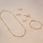 An Endless Summer Bracelet and Necklace in Saint-Tropez laid on sand with four starfishes.