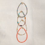 Four Endless Summer Bracelets (Blue Lagoon, Capri, Mykonos and Saint-Tropez) laid vertically on an off-white fabric background. 