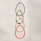 Four Endless Summer Bracelets (Blue Lagoon, Capri, Mykonos and Saint-Tropez) laid vertically on an off-white fabric background. 