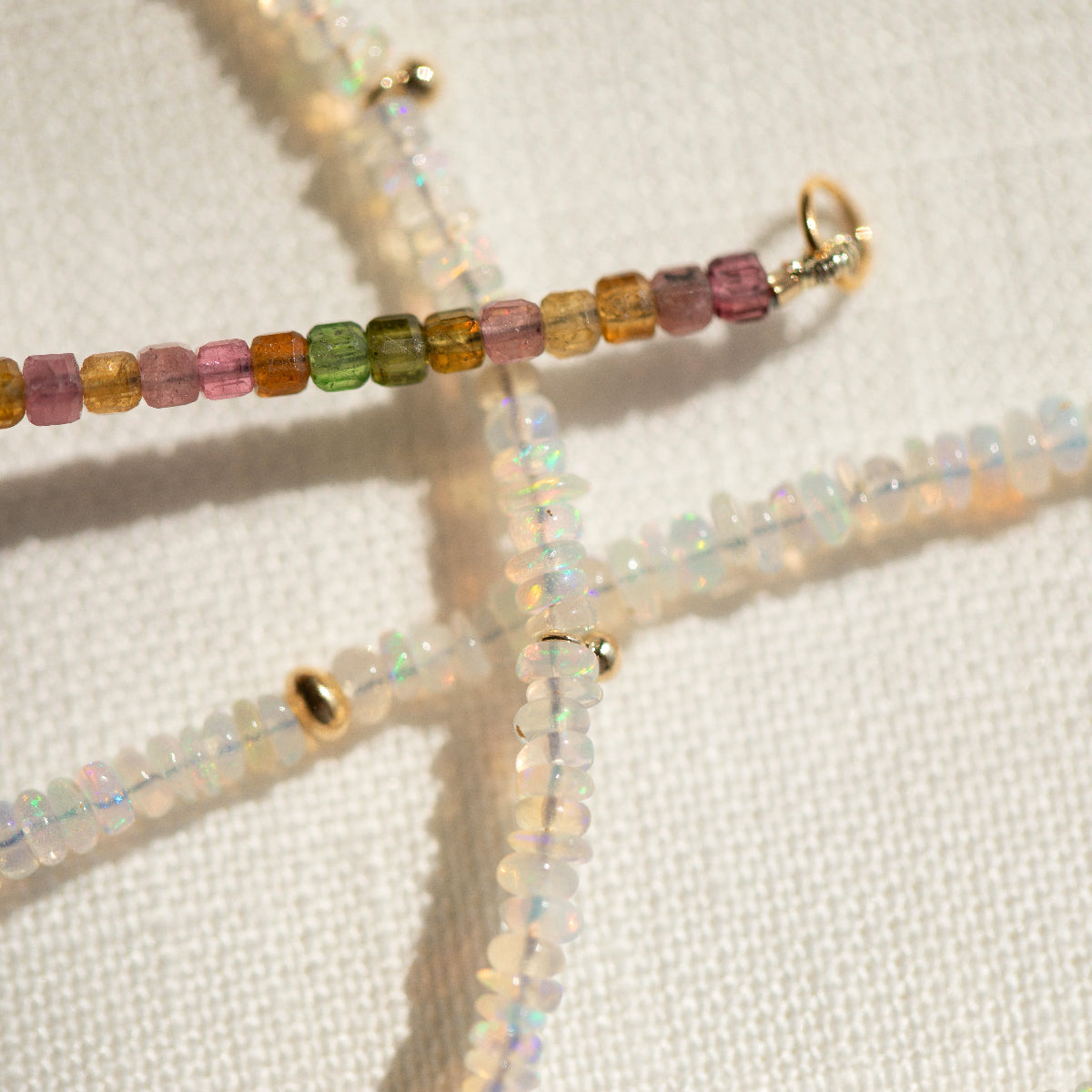 Close-up of two Endless Summer Necklaces on a cream fabric background. 