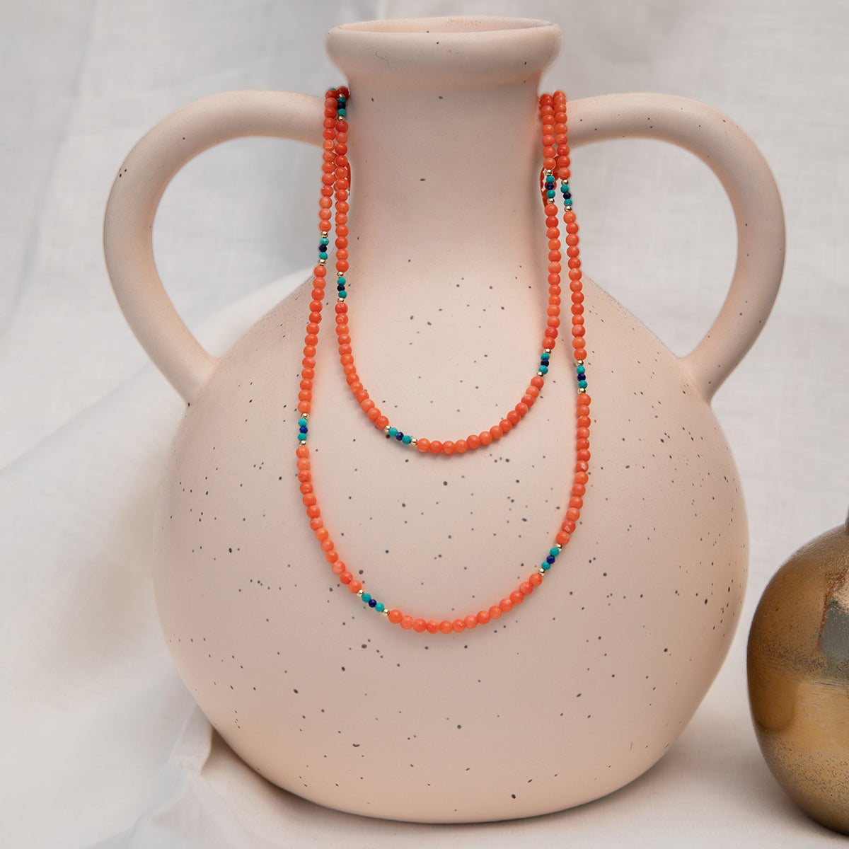 An Endless Summer Necklace - Calypso  draped over a speckled ceramic vase on a white background.