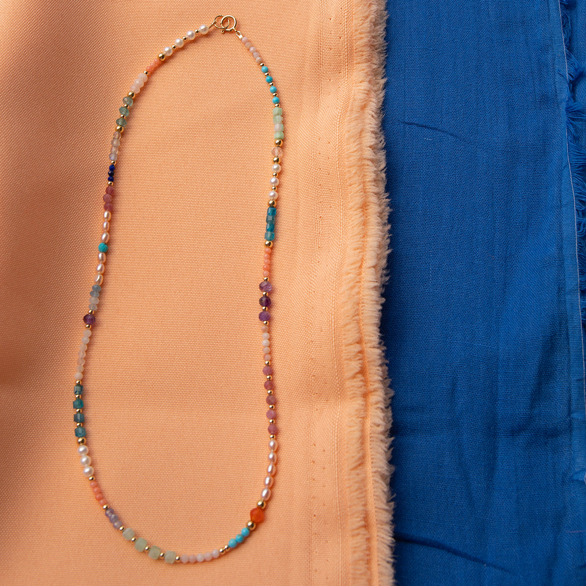 An Endless Summer Necklace - Capri against a blue and orange fabric background. 