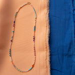 An Endless Summer Necklace - Capri against a blue and orange fabric background. 