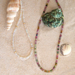Two Endless Summer Necklaces on a sandy background with three shells. 