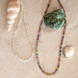 Two Endless Summer Necklaces on a sandy background with three shells. 