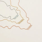 A Pavé MOM Necklace in white gold, a Pavé MAMA Necklace in yellow gold and a Pavé NANA Necklace in rose gold, in a cream background. 