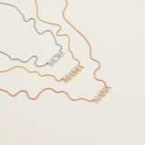 A Pavé MOM Necklace in white gold, a Pavé MAMA Necklace in yellow gold and a Pavé NANA Necklace in rose gold, in a cream background. 