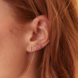 Close-up of a woman's ear wearing a yellow gold Threader Earring Diamond, a Birthstone Stud and a Diamond Bar Earring, with her orange her visible. 