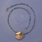 An Endless Summer Necklace - Blue Lagoon and The Golden Venus Shell against a purple background. 