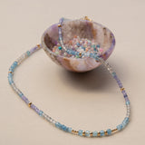 An Endless Summer Necklace - Blue Lagoon laid on top of a small coloured bowl with different coloured beads in it, against a light background.
