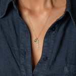 Gold necklace with a blue pendant and diamond 'mommy' pendant worn by a person in a dark shirt.