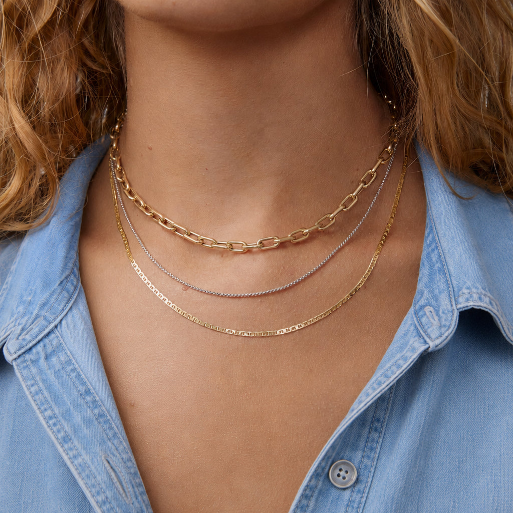 Close-up of a person wearing gold necklaces with a blue denim shirt.